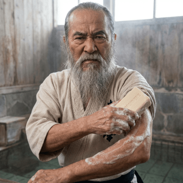 Elderly bearded man washing his arm with Dr. Bronner's soap in a traditional bathhouse.